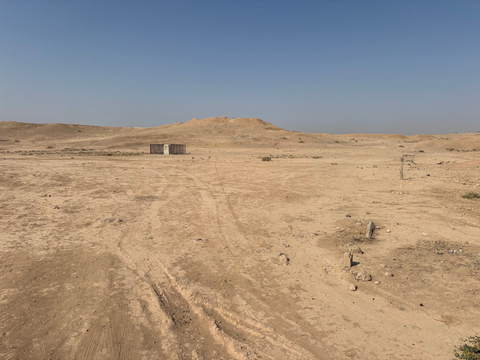 The cemetery seen across open ground. There is no boundary fence and no signage of any kind, and vehicle tracks now run across the burial area.