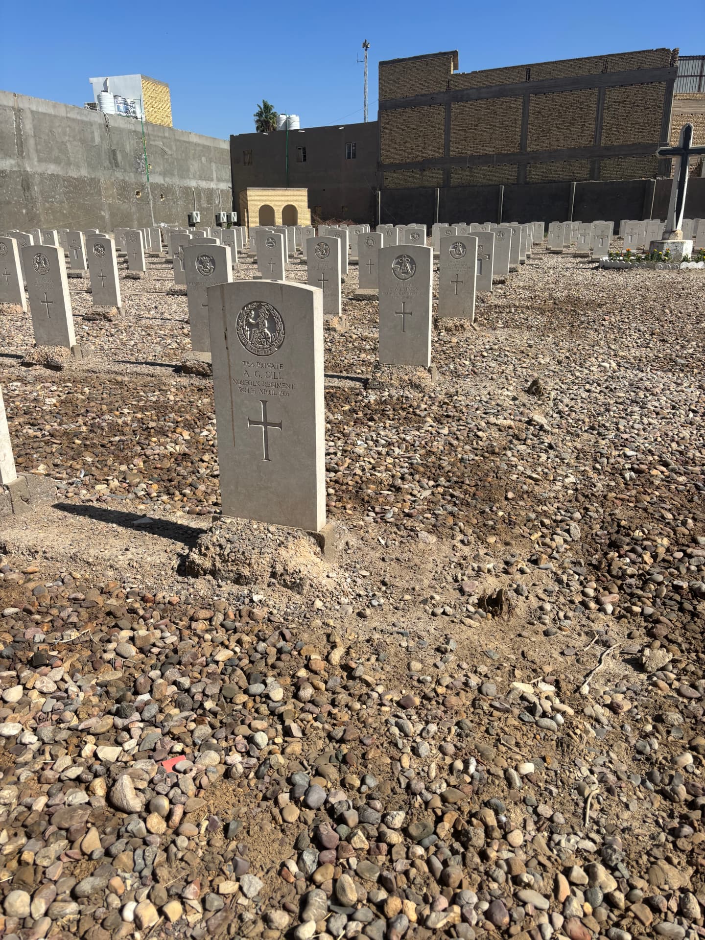 The headstone of 7154 Private A. G. Gill, Norfolk Regiment, died 20 April 1916, standing in disturbed and eroded ground where the gravel surfacing has broken up.