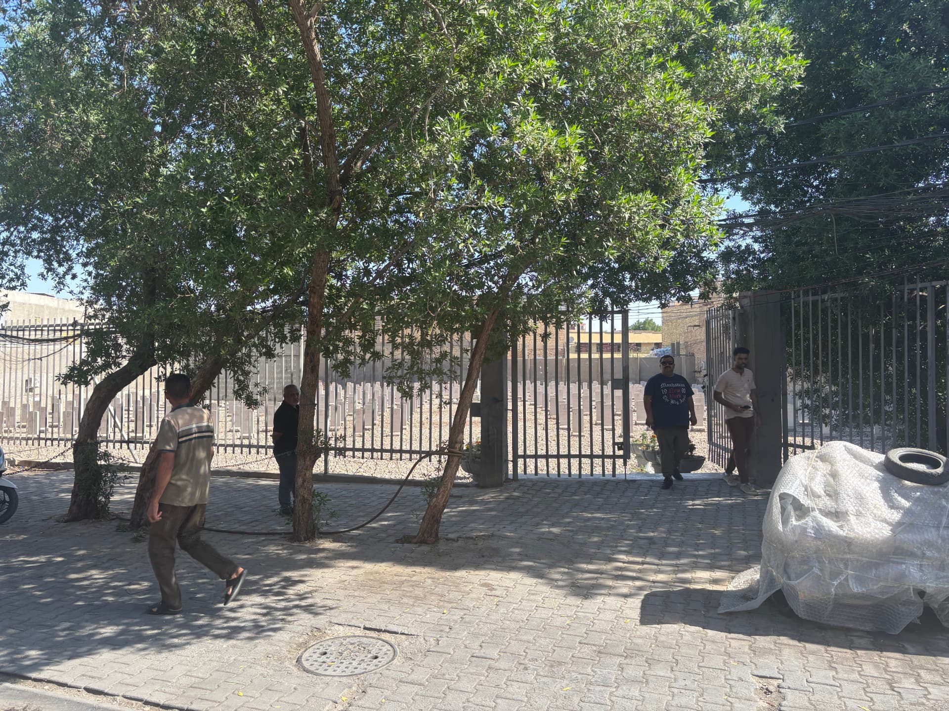 The street frontage of Kut War Cemetery, the railings and gate opening directly onto the town souk with buildings pressing in on three sides.