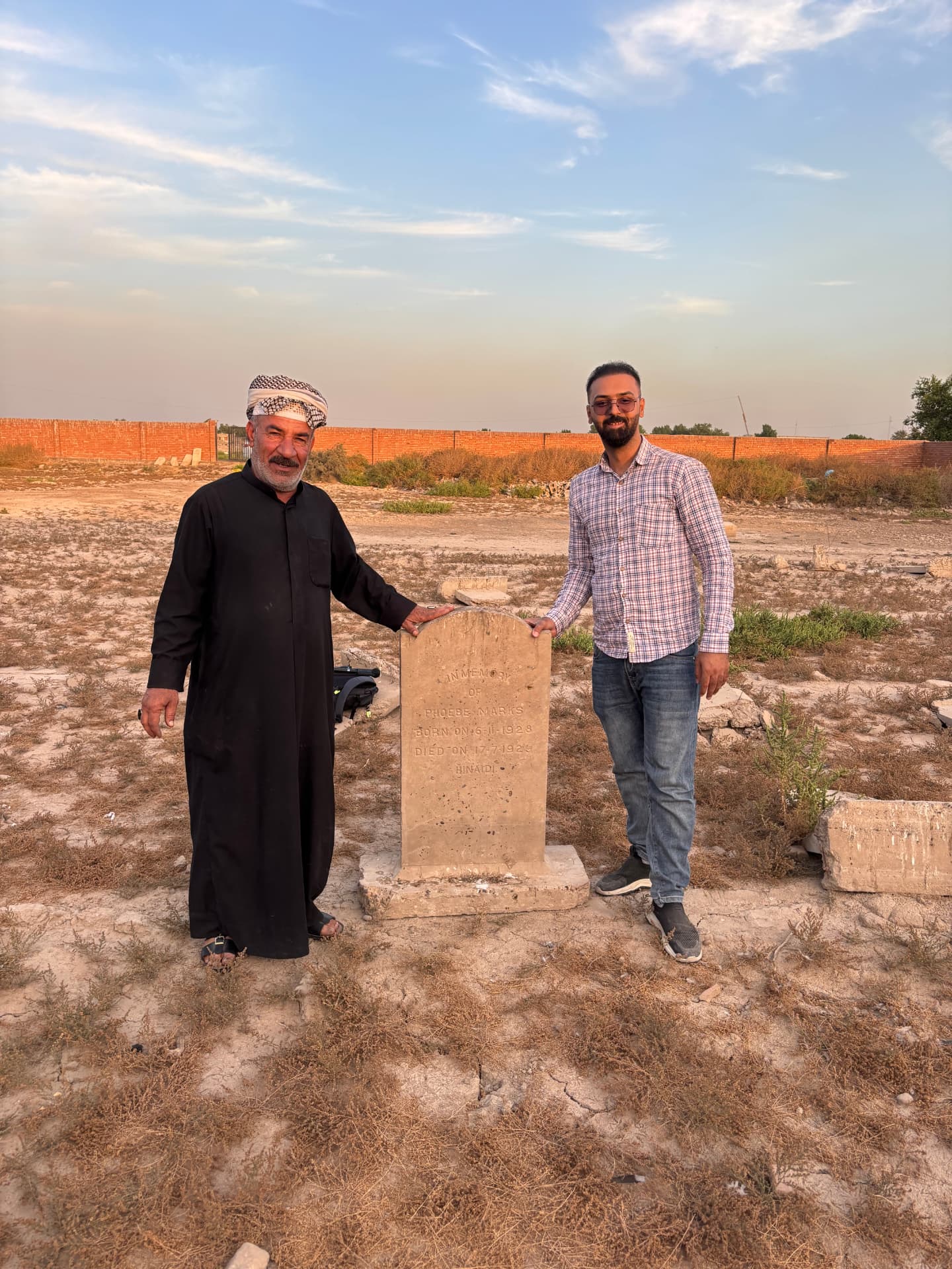 Local custodians beside the re-set headstone of Phoebe Marks, the cleared and largely empty burial ground stretching to the perimeter wall.