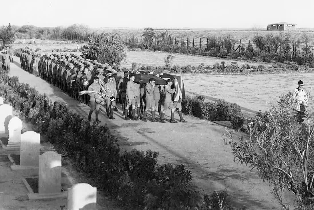 The funeral procession of Aircraftman 1st Class David Arthur Henry Oldfield entering the cemetery, the bearer party carrying the Union Flag draped coffin past a lined route of RAF personnel.