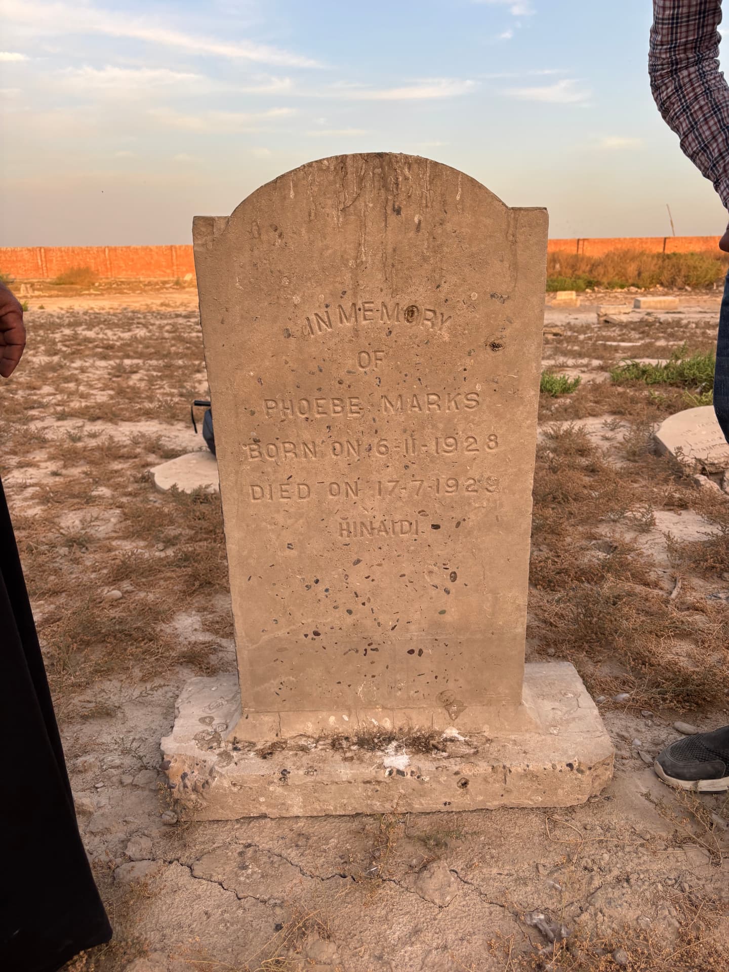 The Phoebe Marks headstone re-set upright on its base, with the cemetery's bare ground and boundary wall behind.