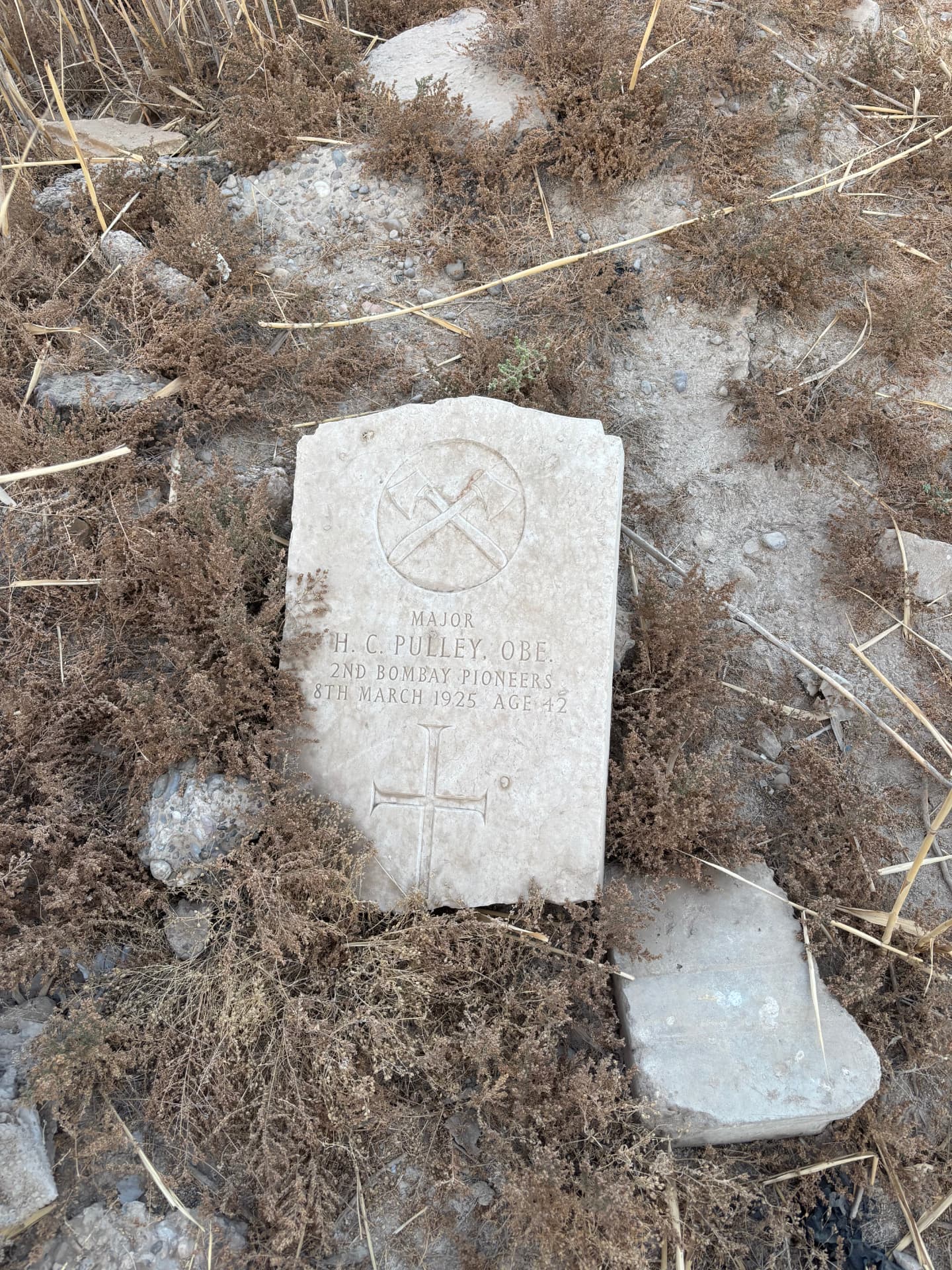 Major H. C. Pulley OBE, 2nd Bombay Pioneers, died 8 March 1925 aged 42. The marble headstone lies flat among dry scrub.