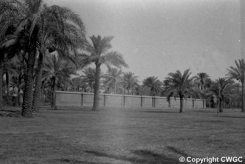 The Memorial Wall set within lawns and palms, erected in the 1930s when the original headstones, destroyed by the saline soil, were removed and the names of all casualties inscribed on permanent screen wall panels. © CWGC.