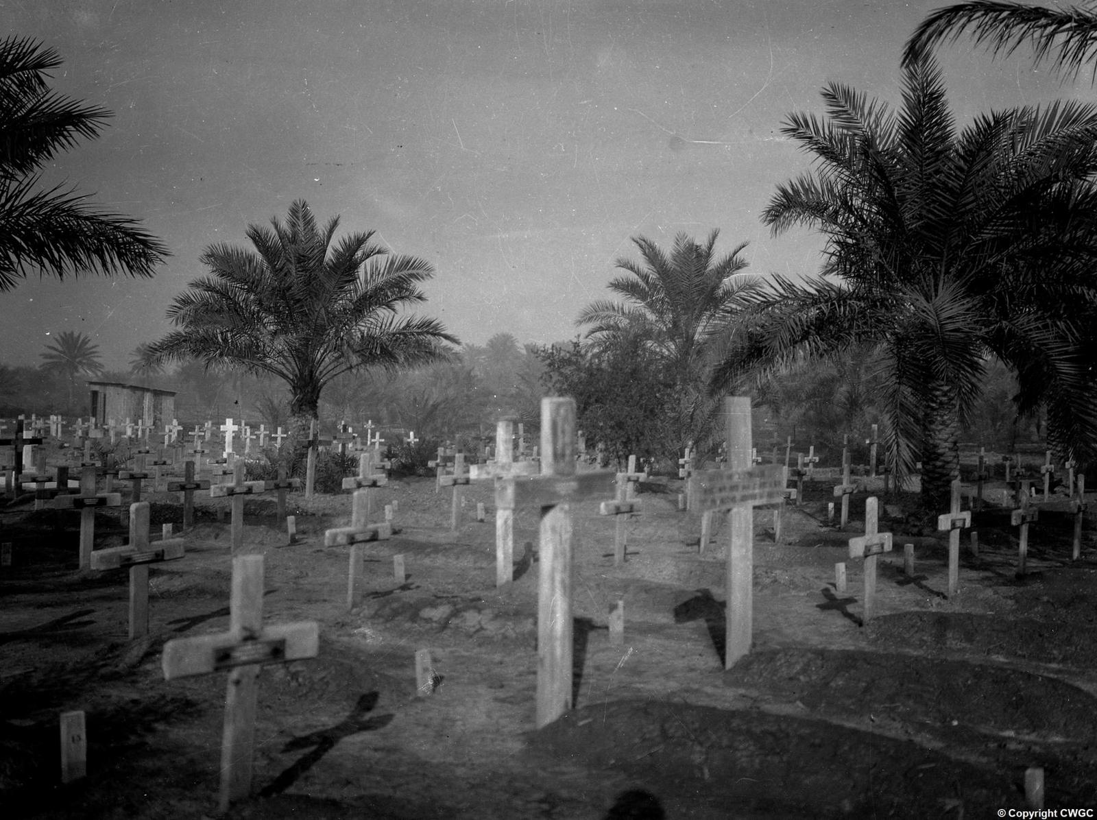 The cemetery prior to its reconstruction, with original wooden and concrete crosses marking individual graves among palms, before the headstones were removed in the 1930s and the names transferred to the Memorial Wall. © CWGC.
