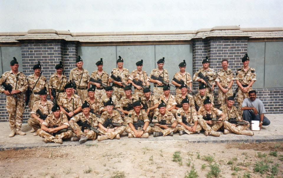 British soldiers photographed in front of the Memorial Wall at Amara War Cemetery, c. 2004, with a local Iraqi staff member kneeling at right.