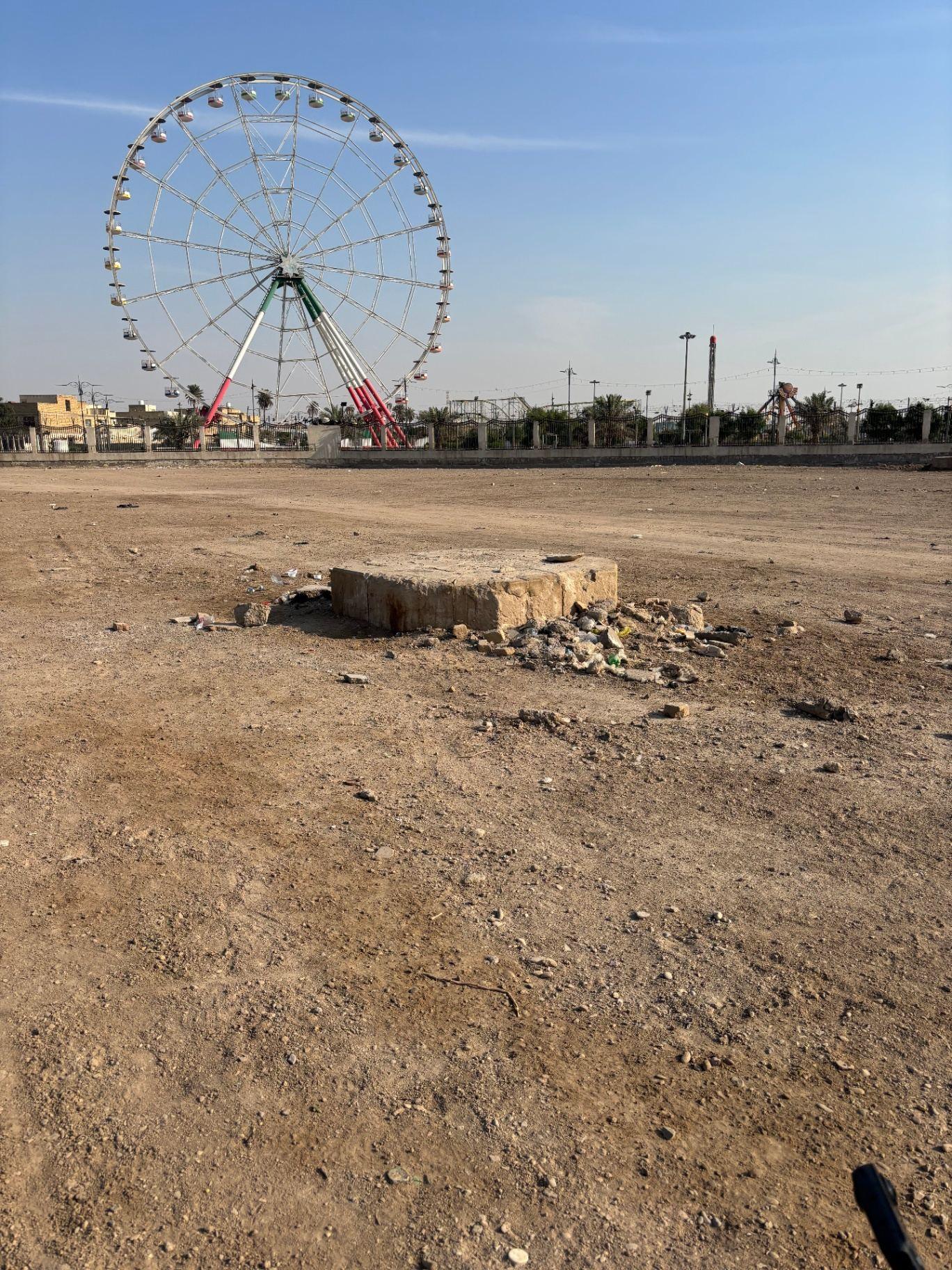The pedestal of the Indian Forces Memorial today, with a ferris wheel and amusement park beyond the cemetery boundary