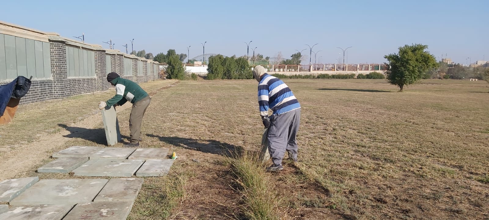 Members of the team carefully lifting and clearing panels from the ground in front of the rebuilt section of the Memorial Wall.