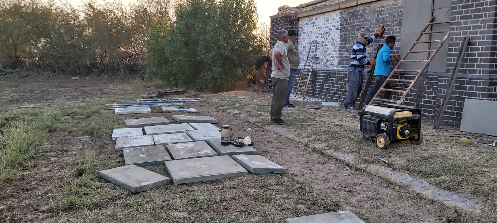 The renovation in progress at sunset: panels staged on the ground while the team works on the rebuilt brick wall in the background.
