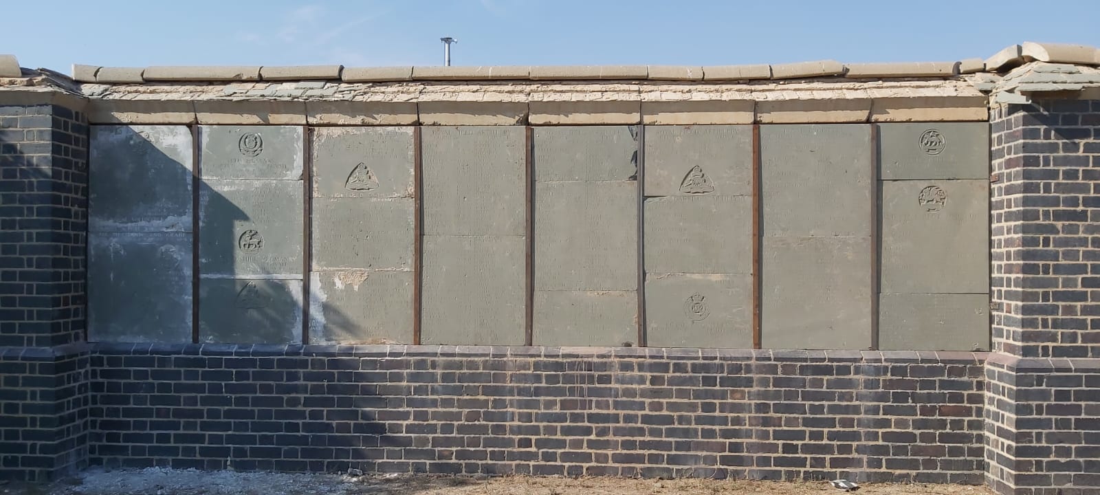 A completed section of the renovated Memorial Wall, with regimental crests and inscribed panels reset between brick piers.
