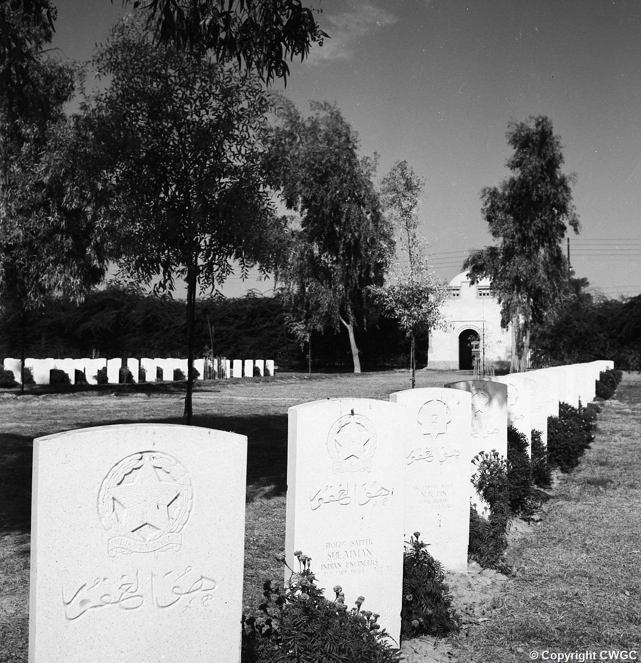 Headstones inscribed in Arabic and bearing the Indian Engineers badge, including that of Sapper Sulaiman, Indian Engineers, killed August 1944. The Cremation Memorial gatehouse is visible in the distance. © CWGC.