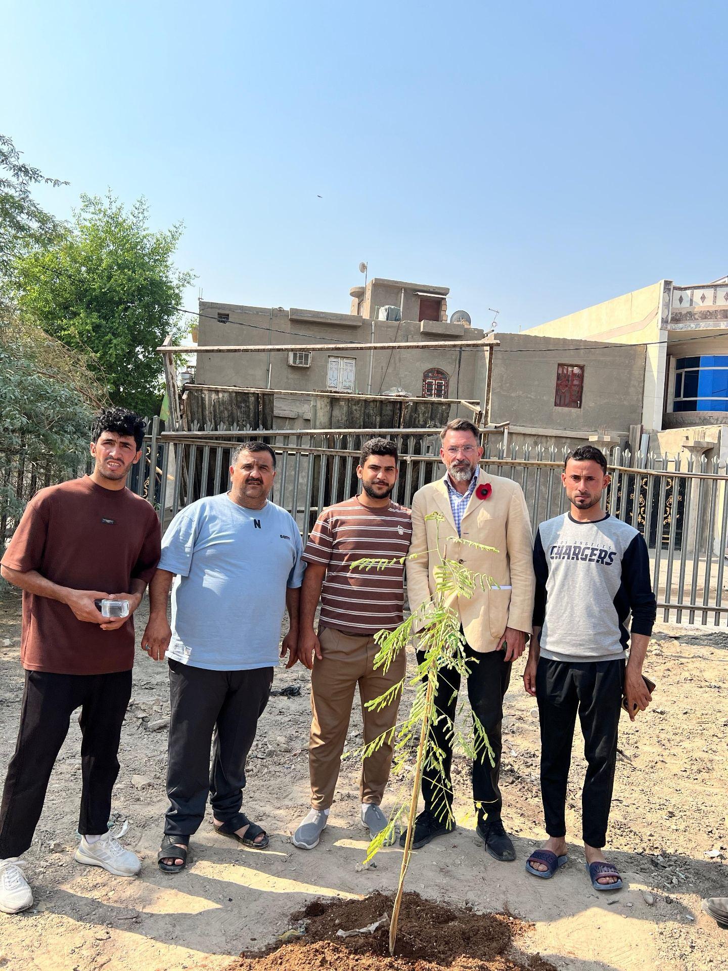 Hasan and his friends from the Al Hakameia neighbourhood standing with the author beside a newly planted sapling on the grounds of Basra War Cemetery.