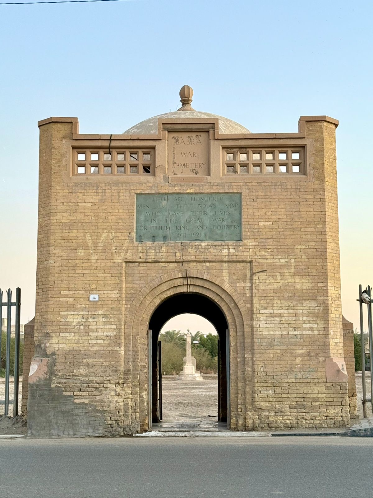 The main gatehouse of Basra War Cemetery, with its dedication panel "Here are honoured men of the Indian Army who gave their lives in the Great War for their King and country, 1914-1921" set above the arched entrance, and the Cross of Sacrifice visible in the distance through the open doorway. Photo: Shane Potaka.
