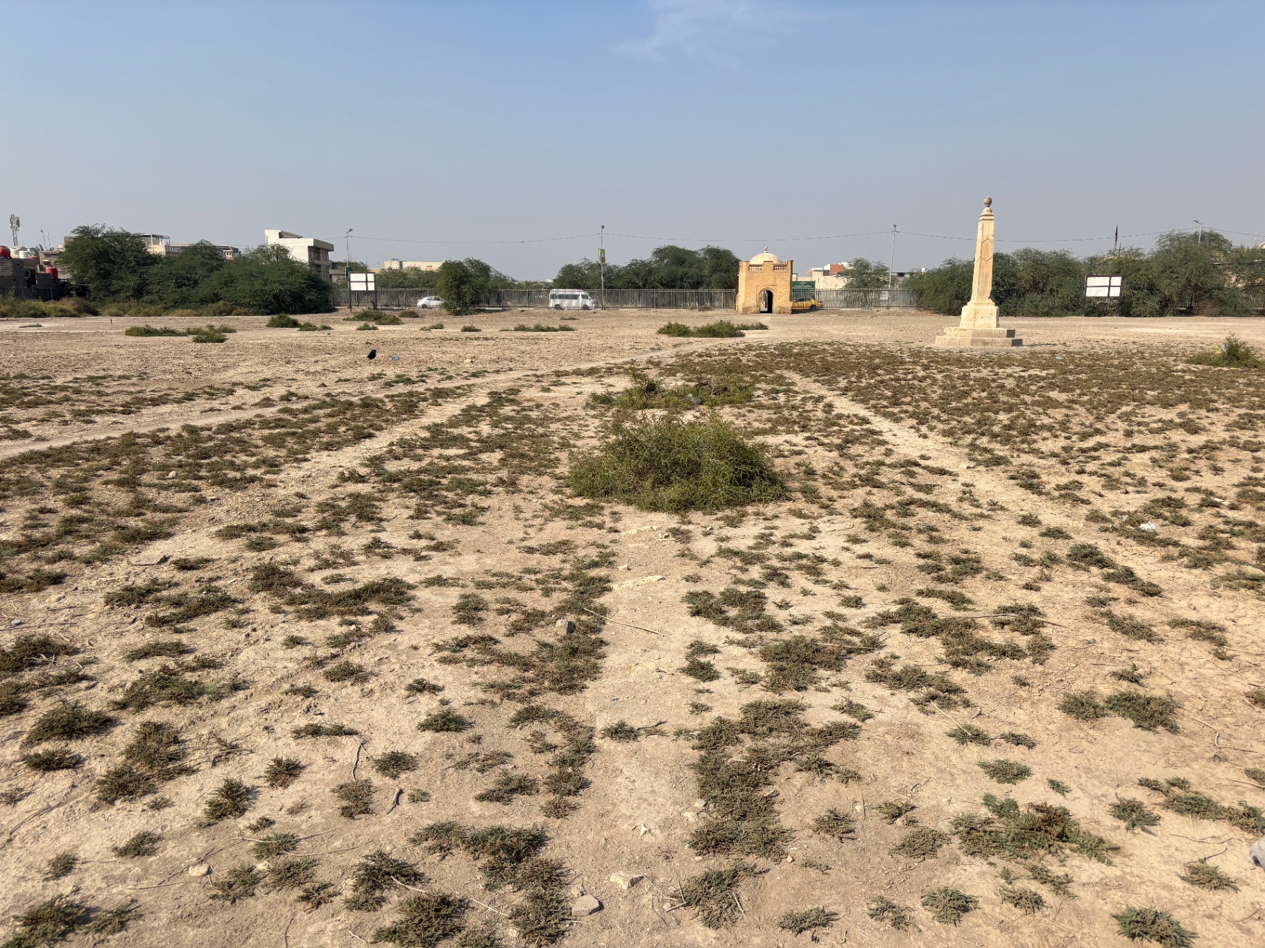 The Indian Forces side of Basra War Cemetery today, with the obelisk standing at right and the Cremation Memorial gatehouse visible in the distance, the grave plots reduced to bare ground and scrub. Photo: Shane Potaka.