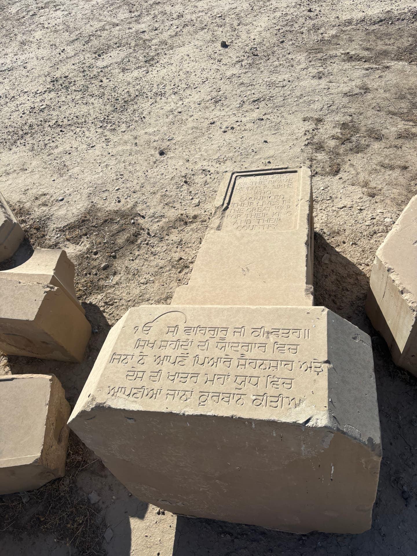 The shaft and base of the Hindu and Sikh memorial lying flat in the dirt, the English dedication and the Gurmukhi inscription to the Sikh fallen still clearly legible.