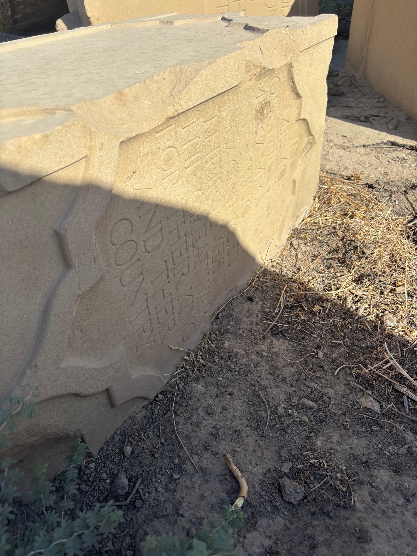 A broken inscription block, its lettering chipped away along the fractured edge where the stone has been struck and split.