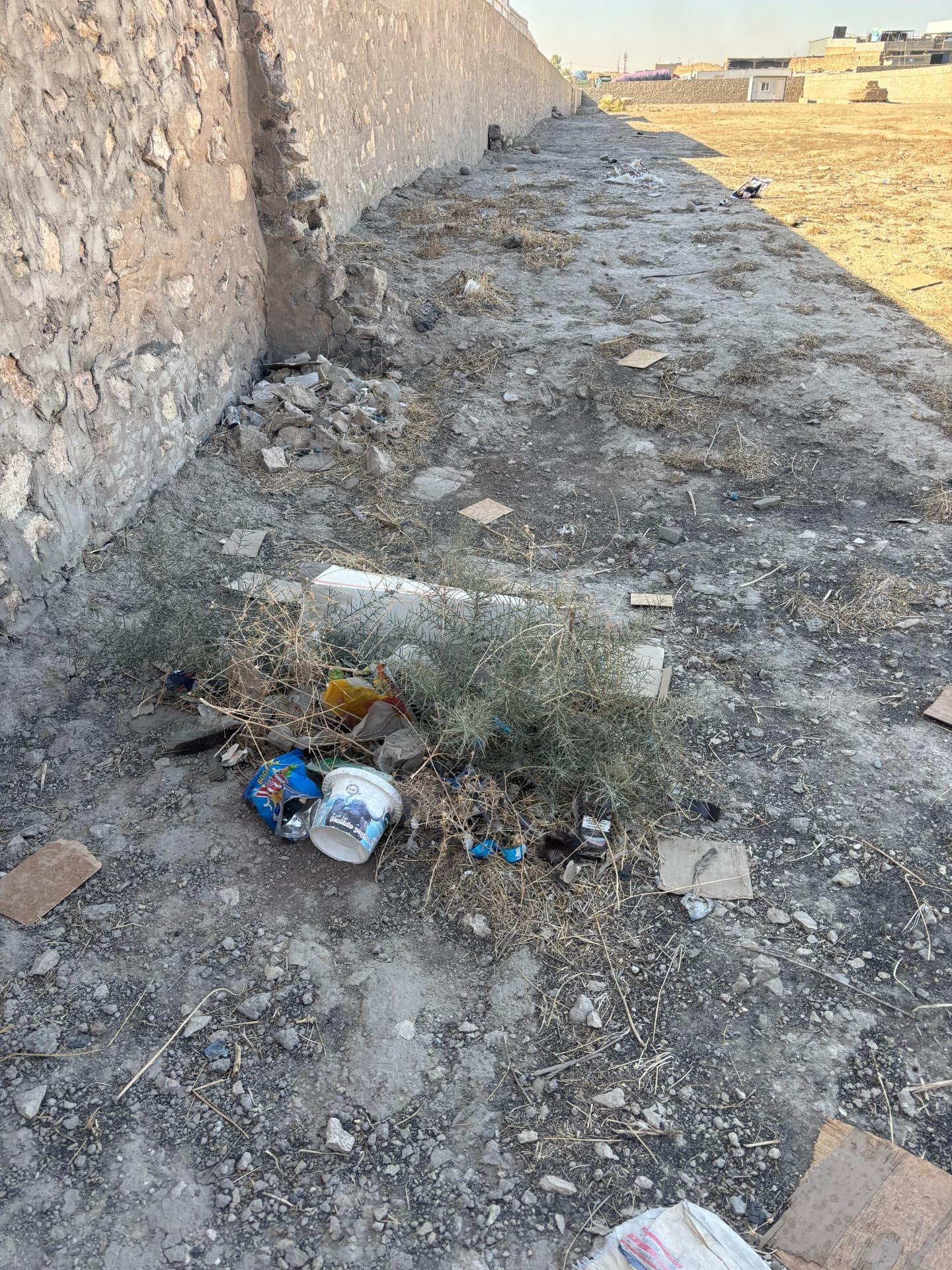 Rubbish, tumbleweed and broken tiling collecting along the inside of the perimeter wall.