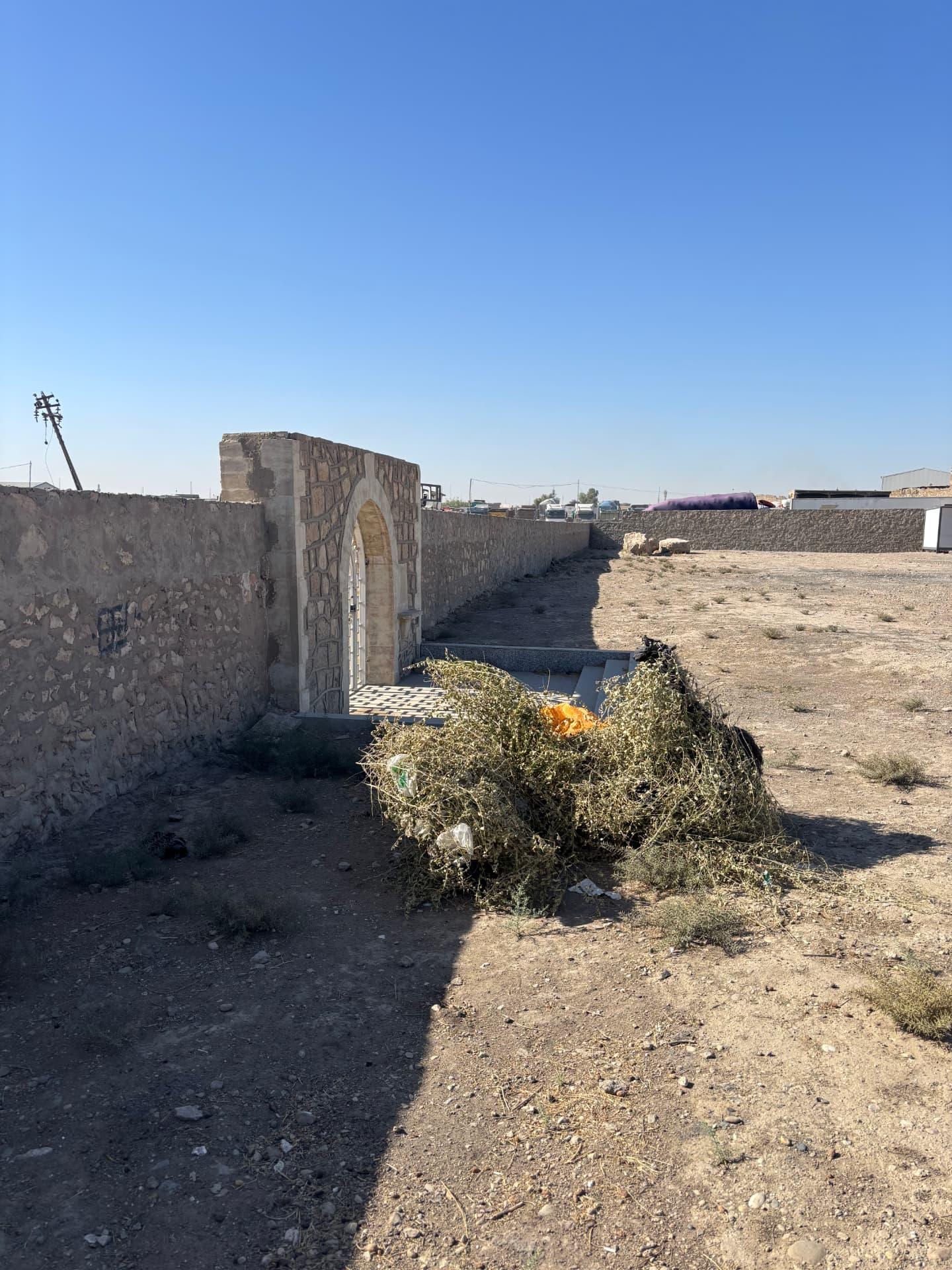 The new gate and perimeter wall built by the contractor, with cut vegetation and rubbish piled against the entrance path.