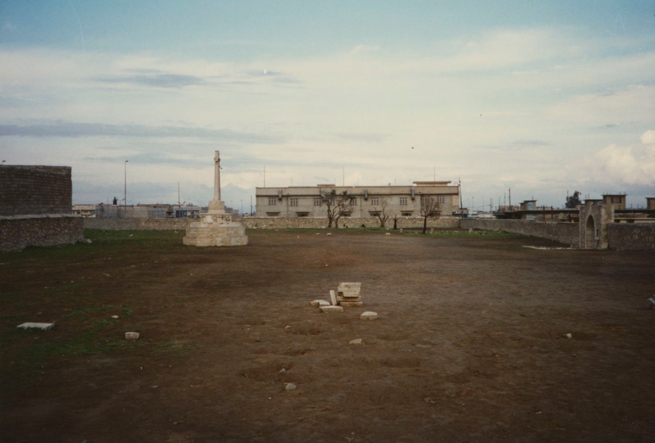 Mosul War Cemetery in 1987, the headstones already gone and the Cross of Sacrifice standing on bare ground, with only scattered fragments of stone remaining.
